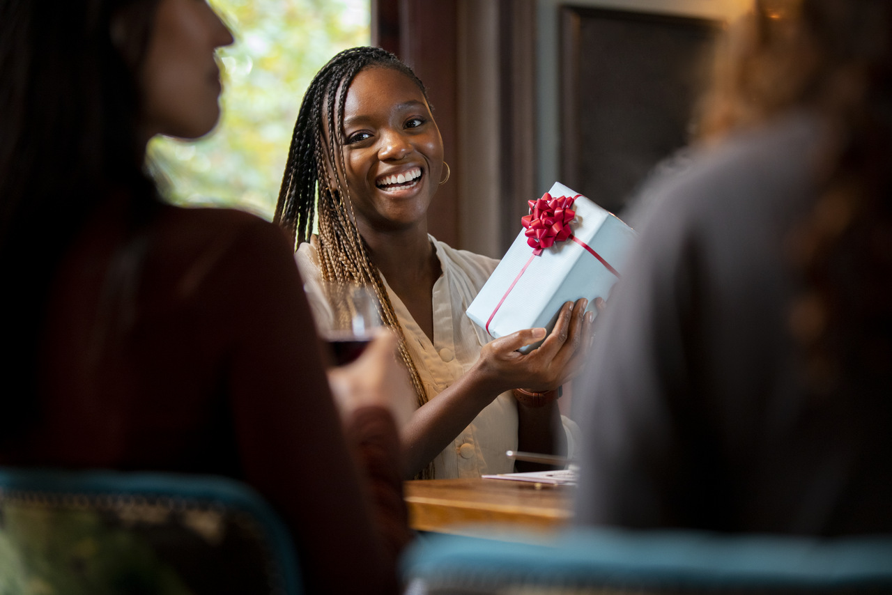 A woman smiling as she holds out a gift box at a table